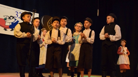 
                                        Dzieci z zespołu ludowego chłopcy ubrani w czarne czapki białe koszule i czarne spodnie dziewczynki ubrane w kolorowe sukienki                                        