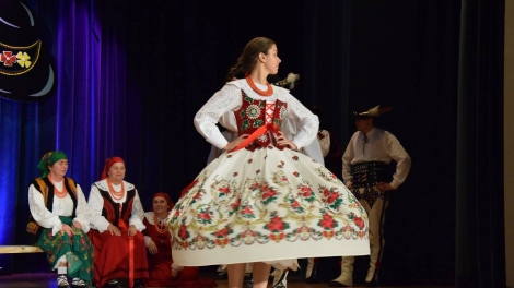 
                                        Pani w białej koszuli czerwonej kamizelce i kolorowej spódnicy tańczy na scenie                                        