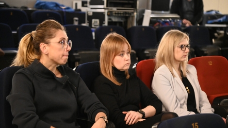 
                                        Na widowni siedzą trzy panie w blond włosach dwie panie w czarnych sukienkach pani z prawej strony w białym żakiecie                                        