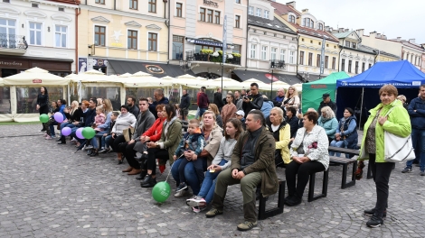
                                        Publiczność siedzi na rynku przed sceną                                        
