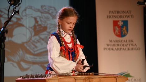 
                                        Dziewczynka gra na cymbałkach ubrana w rzeszowski strój ludowy                                        
